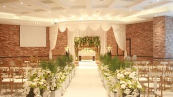 A wedding venue with a central aisle, floral arrangements, and a brick wall backdrop.