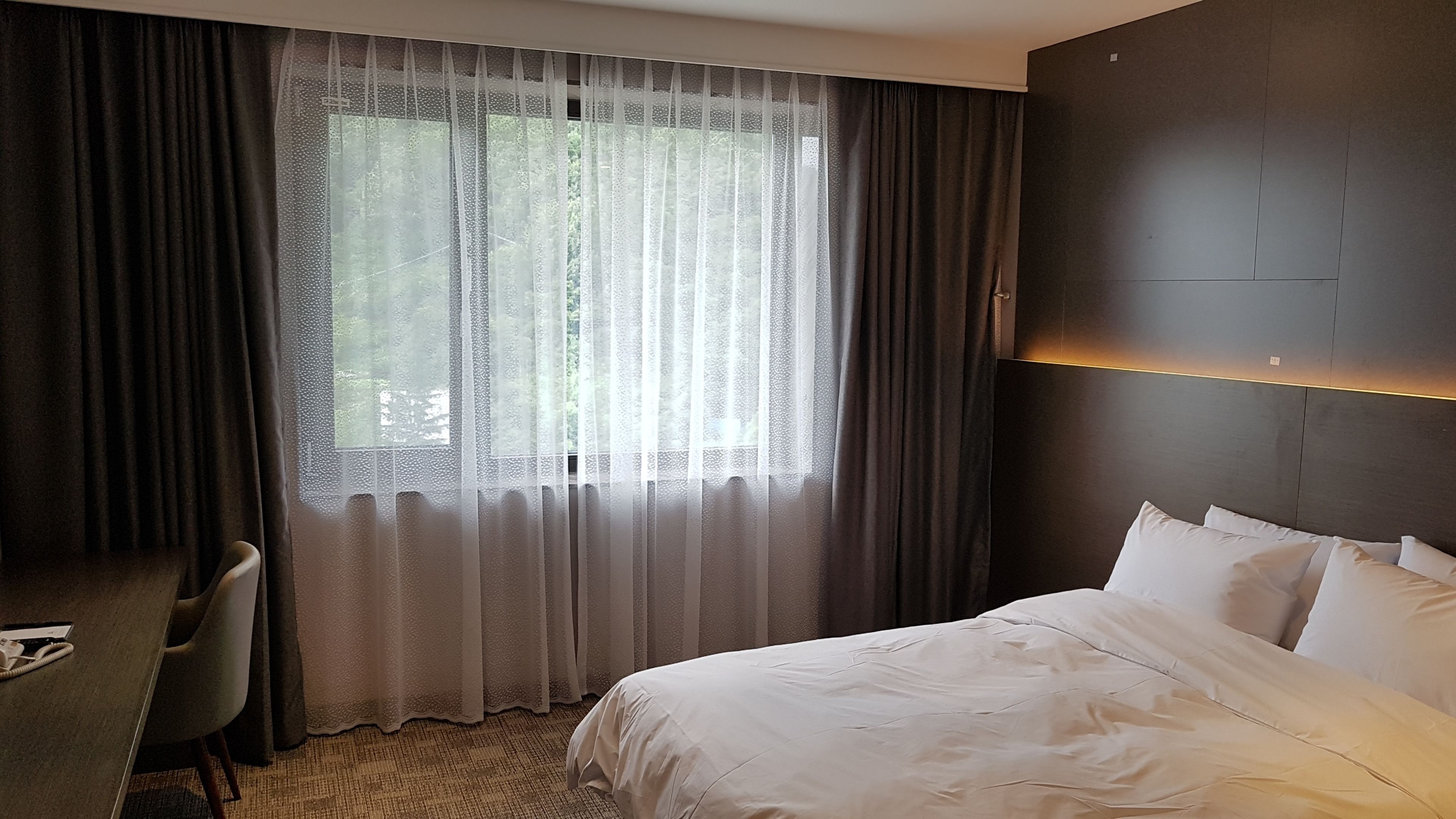 Une chambre d’hôtel avec un grand lit, un bureau et une fenêtre avec des rideaux légers.