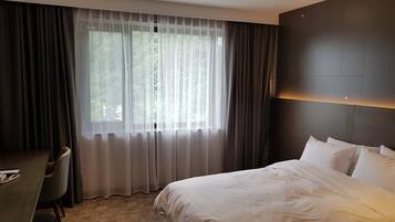 Une chambre d’hôtel avec un grand lit, un bureau et une fenêtre avec des rideaux légers.