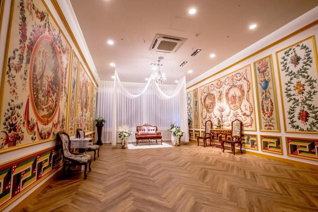 A room with a wooden parquet floor, a central seating area with a sofa and chairs, and walls adorned with floral and geometric patterns.