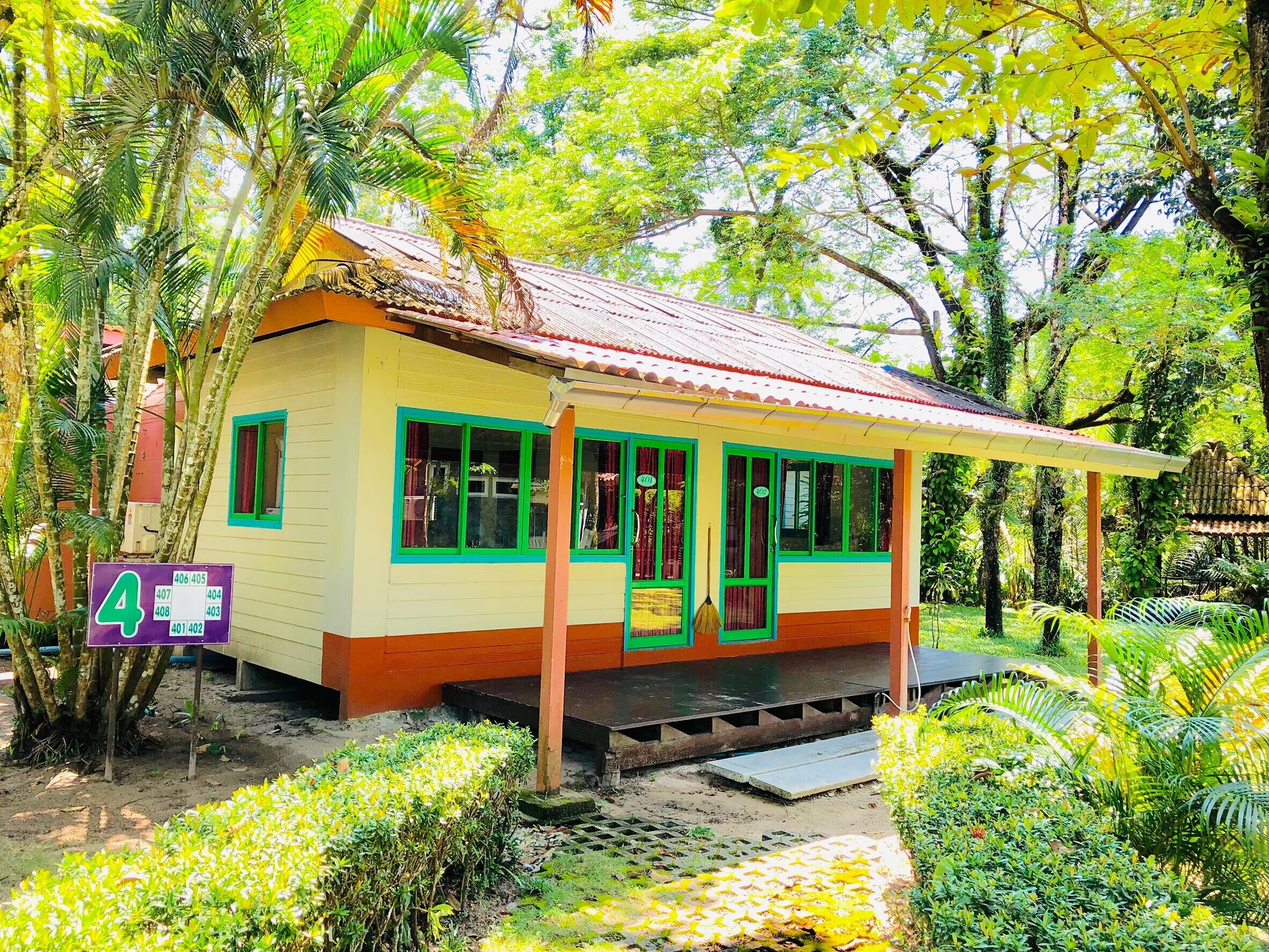 A small, single-story building with a sloped roof, green-framed windows, and a porch.