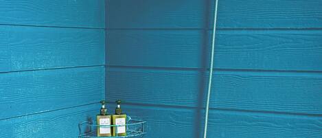 A bathroom with a blue wooden wall, a shower with a handheld showerhead, and a glass shelf with two bottles.