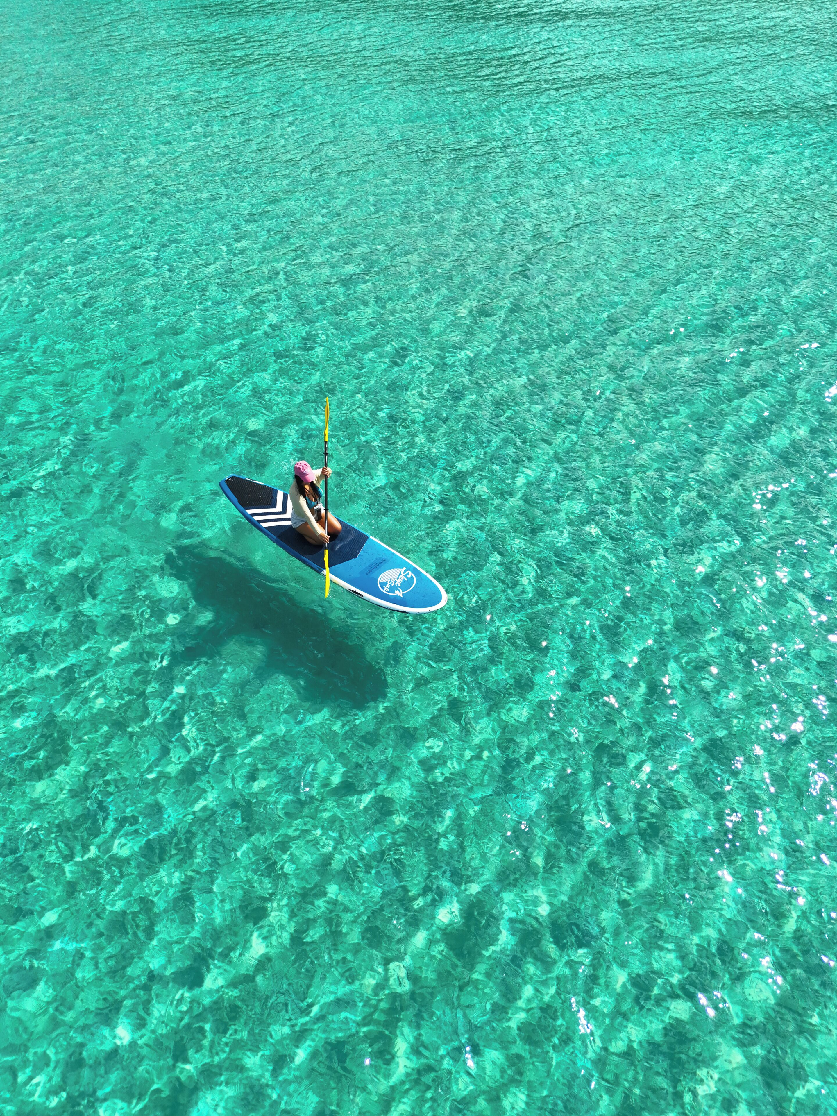 Iemand zit op een surfplank in helder turquoise water.