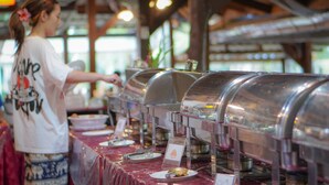 A buffet setup with covered food dispensers, a table with plates, and a person serving food. - Ko Kut Ao Phrao Beach Resort (Ko Kood)