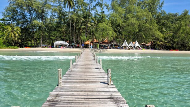 A wooden pier leading to a beach with clear water, surrounded by palm trees and beach huts. - Ko Kut Ao Phrao Beach Resort (Ko Kood)