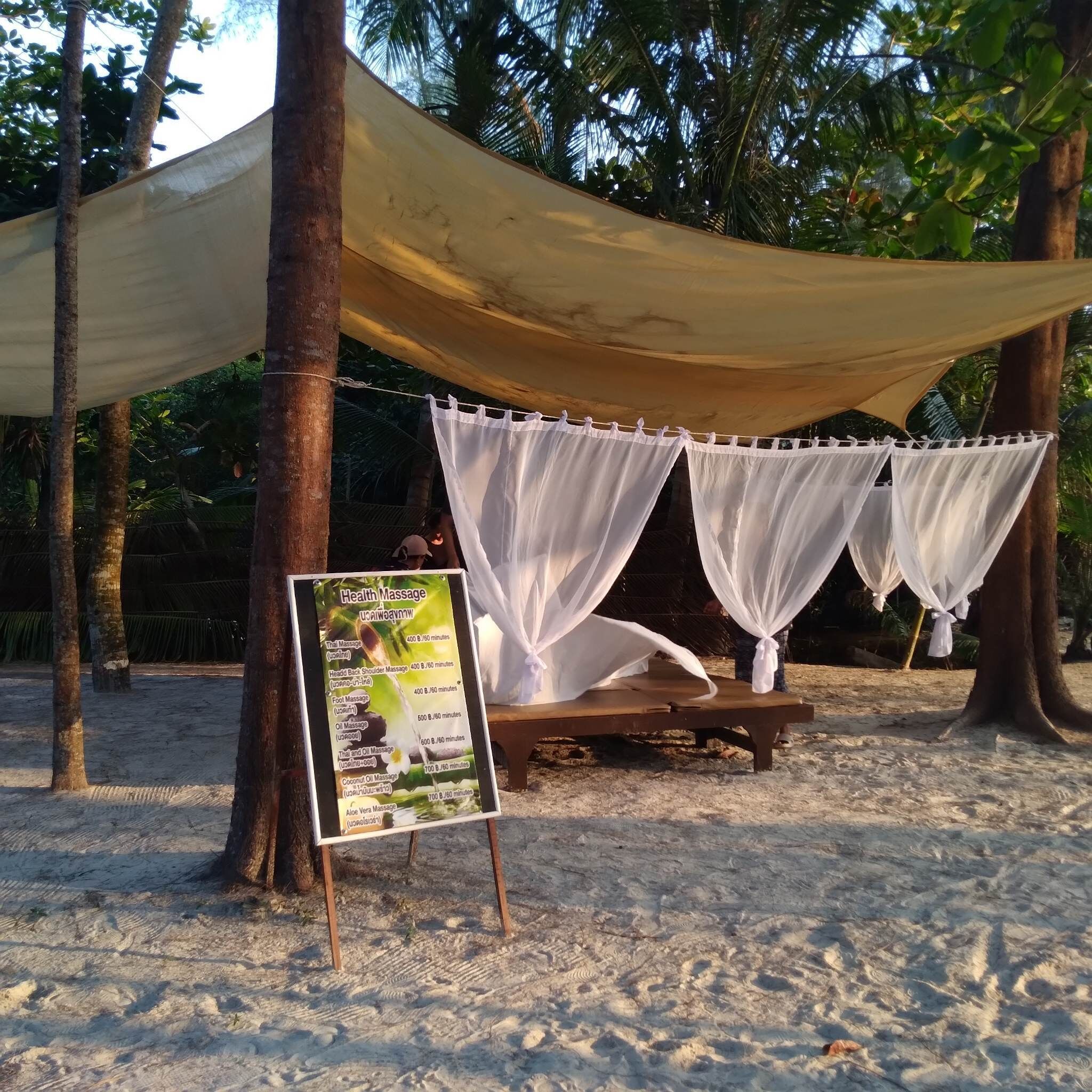 A beachside massage tent with a sign listing services and prices.