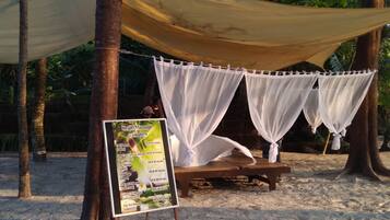 A beachside massage tent with a sign listing services and prices.