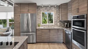 A modern kitchen with stainless steel appliances, a stone backsplash, and wooden cabinets.