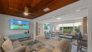A spacious living room with a wooden ceiling, a large flat-screen TV, a sofa set, and a coffee table.