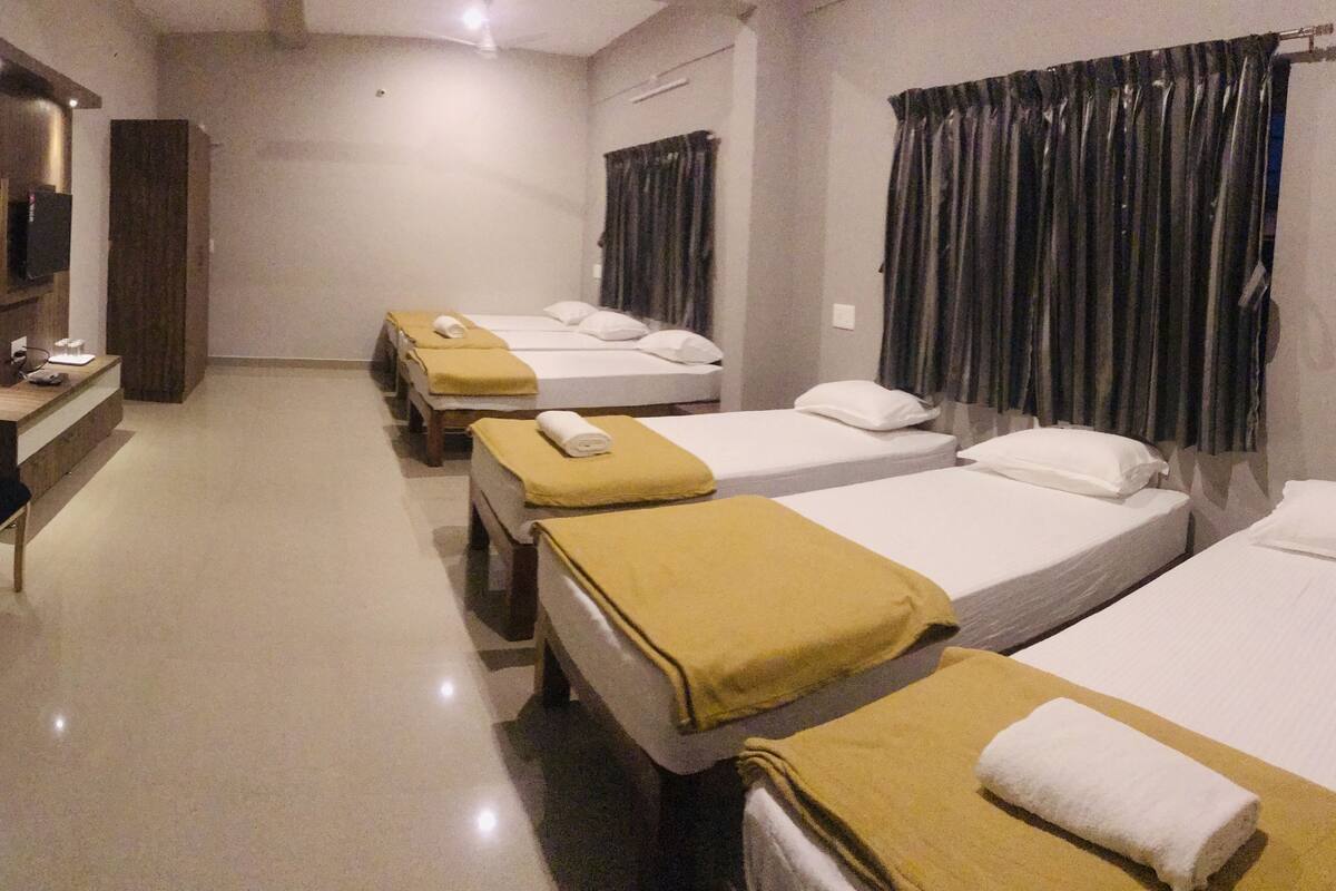 A hotel room with four single beds, a desk with chairs, and a television on the wall.