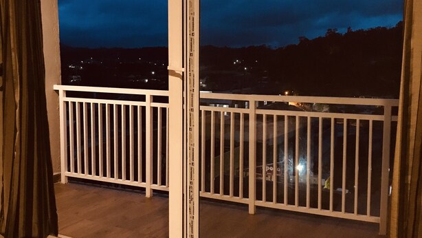 Un balcó amb barana blanca, vista del cel nocturn i un paisatge urbà al fons.