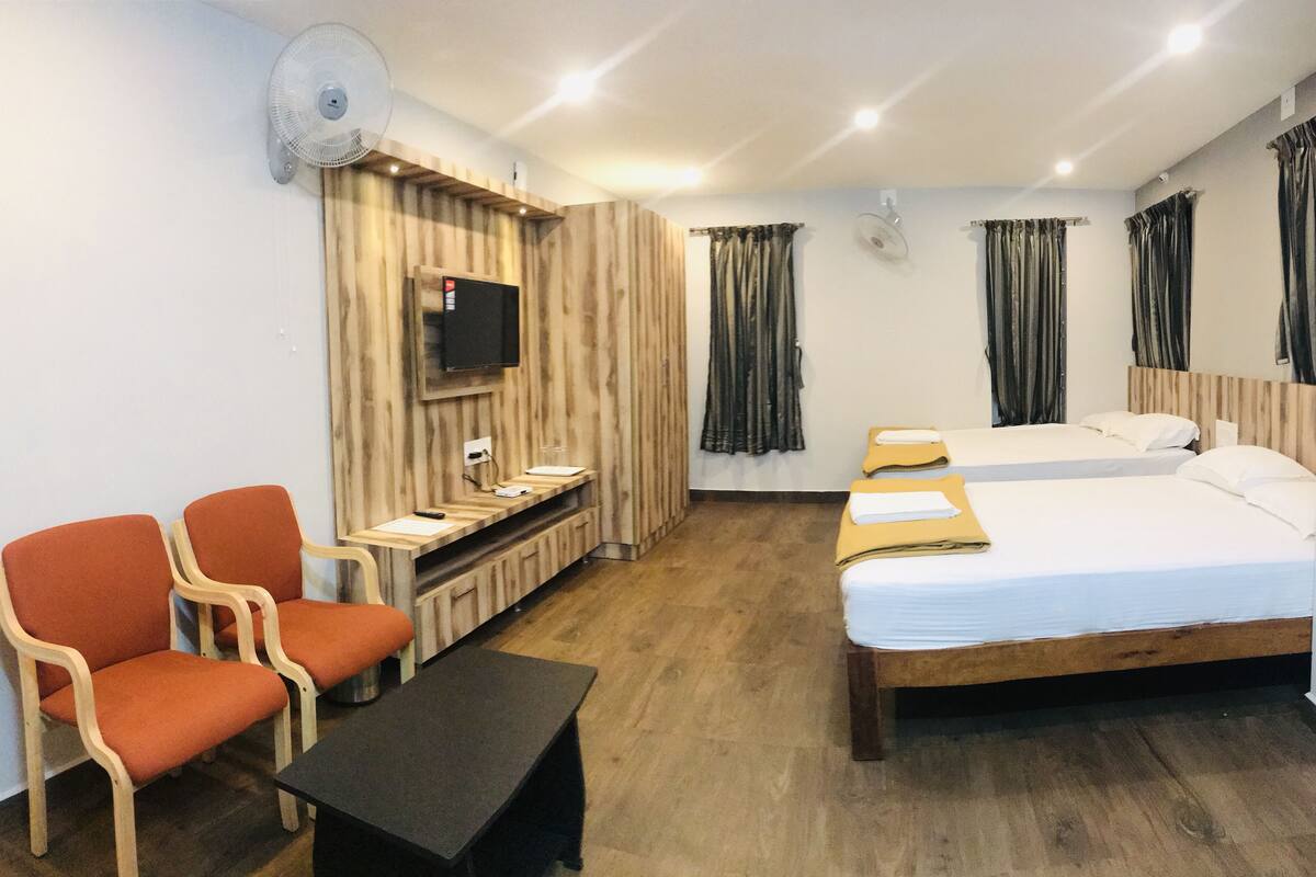 A hotel room with a bed, two orange chairs, a small table, a TV, and curtains.