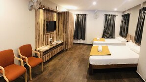 Habitació d'hotel amb dos llits, una taula de treball, un televisor i cadires taronja.