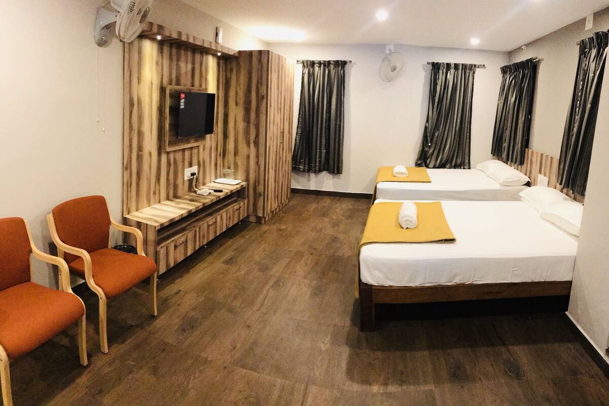 A hotel room with two beds, a desk, a TV, and orange chairs.