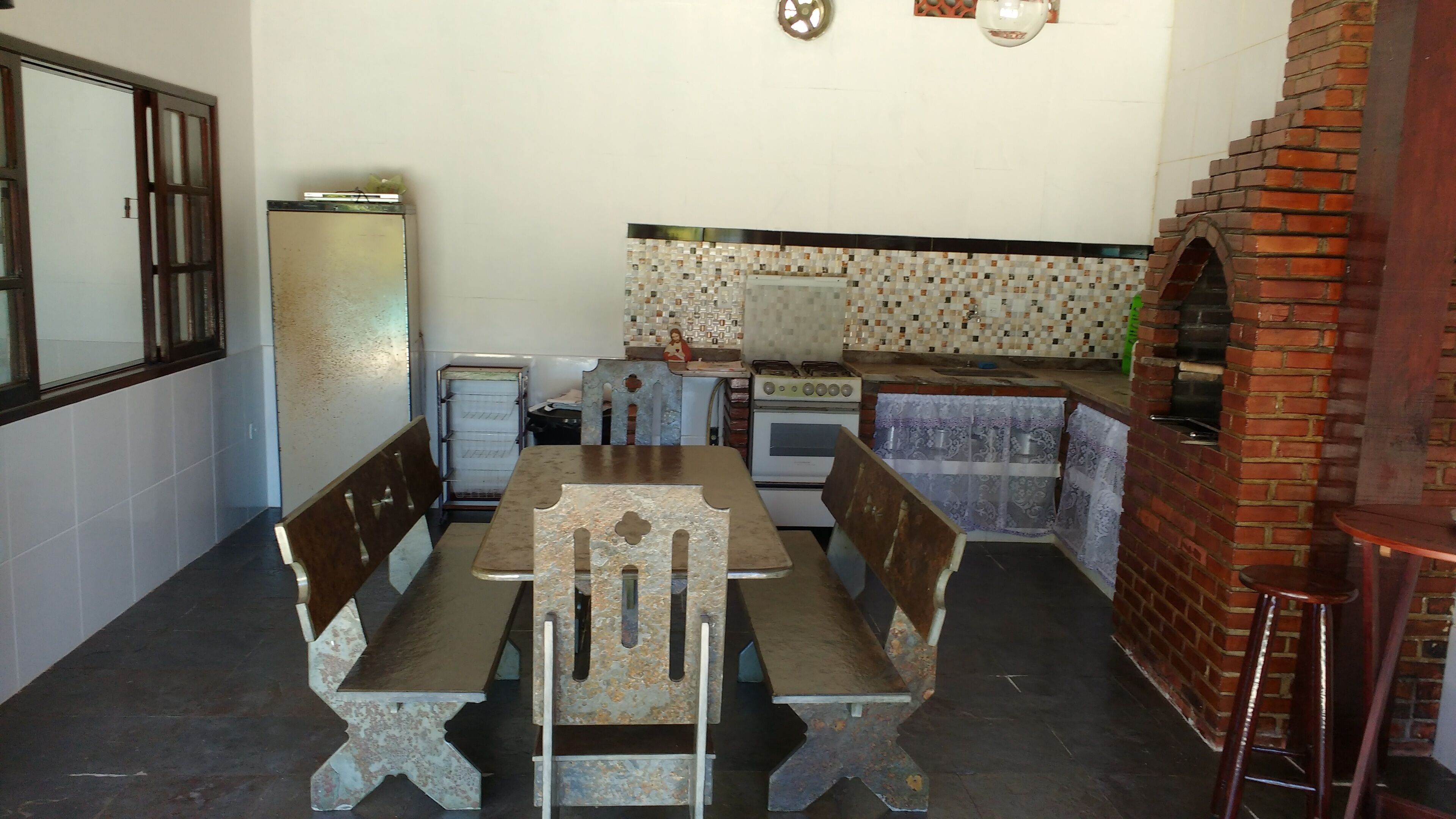 Uma cozinha compacta com mesa e bancos, geladeira, fogão e forno de tijolos.