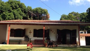 Una casa con tetto in tegole, un portico con panchine e un cane nel giardino.