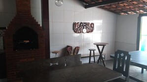 Un ristorante con camino in mattoni, soffitto in legno e parete rivestita in piastrelle con un orologio. Si notano due sgabelli e un tavolo con sedie.