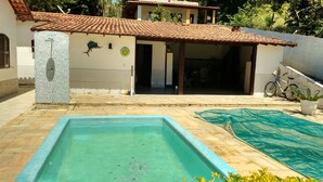 Una piscina con bordo piastrellato, una bicicletta e un edificio con tetto e decorazioni murali piastrellati.