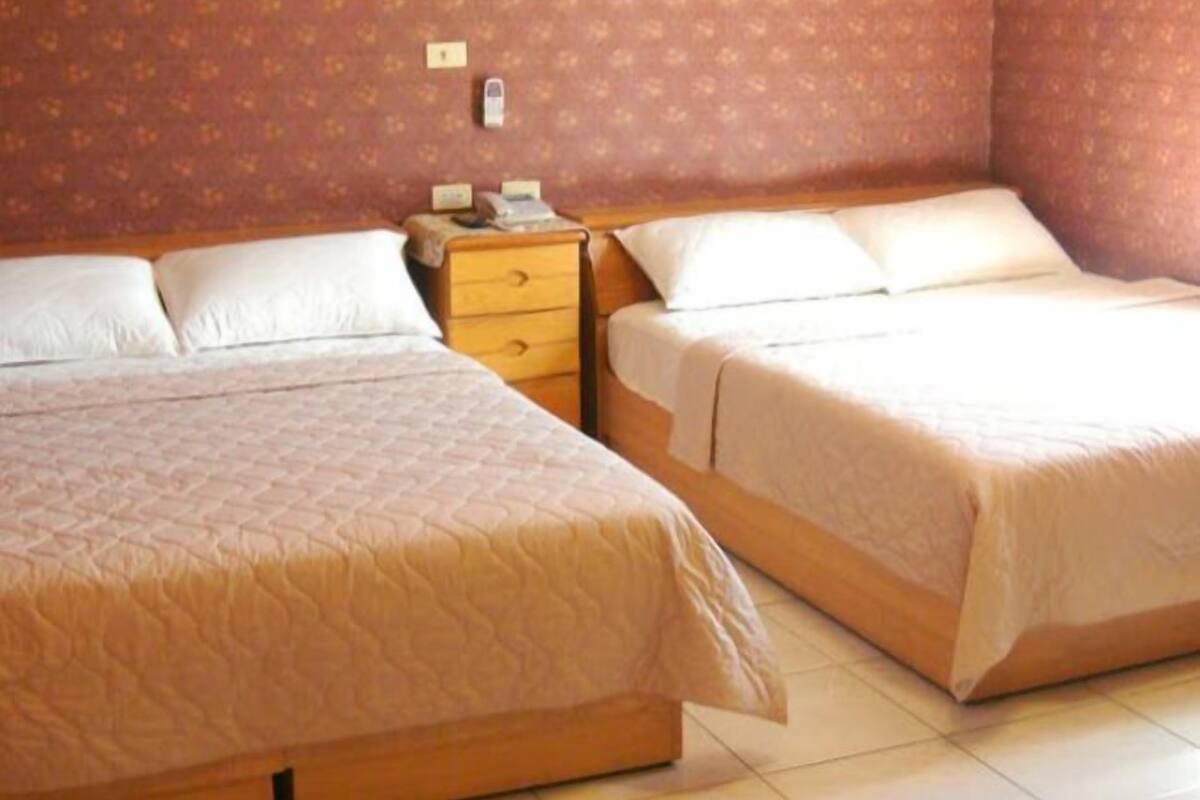 Quarto de hotel com duas camas, uma mesa de cabeceira e um telefone fixado na parede.