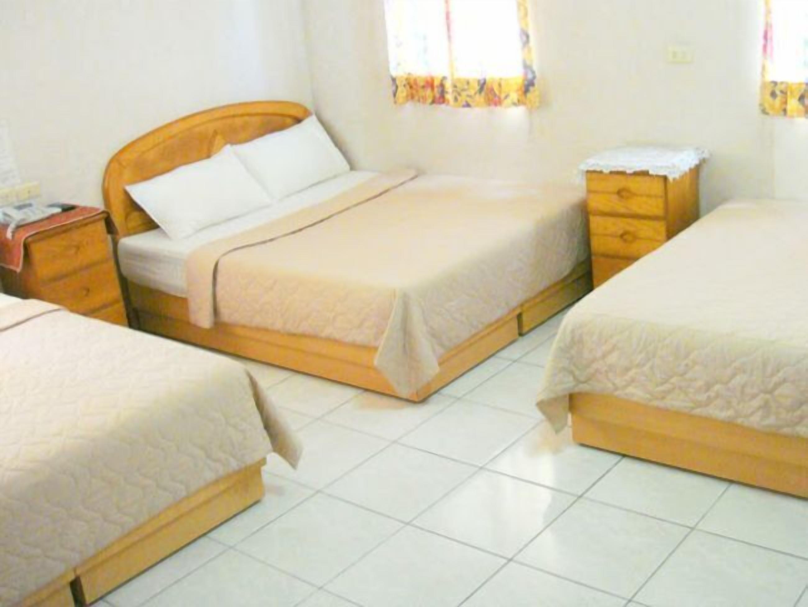 A room with two beds, wooden headboards, a nightstand, and a small dresser.