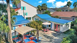 A two-story house with a blue roof, a covered patio with outdoor furniture, and a small garden area.