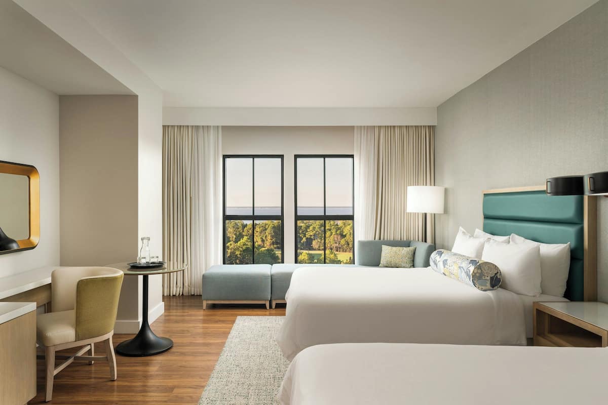Une chambre d’hôtel équipée d’un lit, d’un bureau, d’une chaise et offrant une vue sur l’extérieur grâce à de grandes fenêtres.