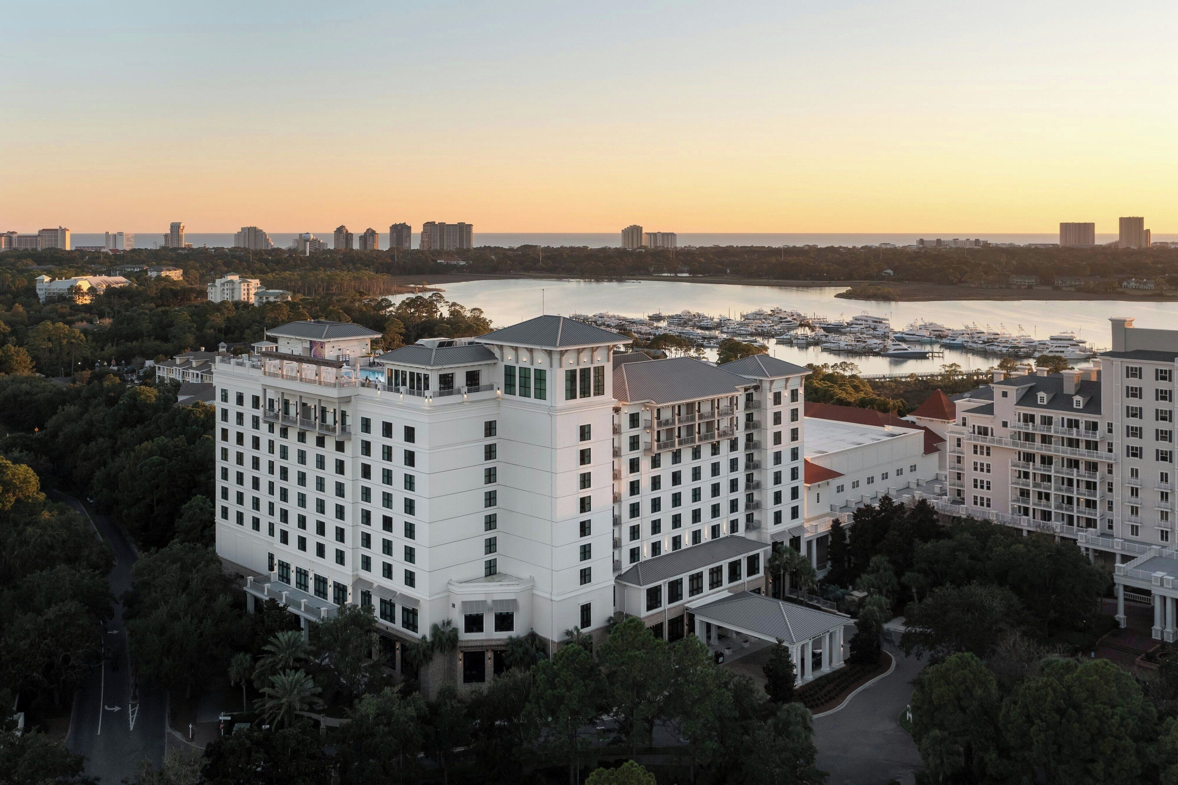 A high-rise hotel with multiple floors, surrounded by lush greenery and a marina with boats.