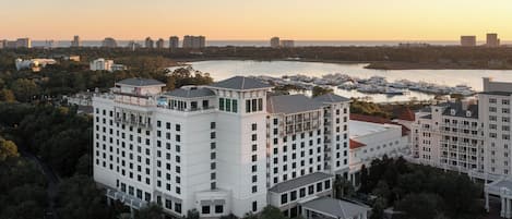 A high-rise hotel with multiple floors, surrounded by lush greenery and a marina with boats.