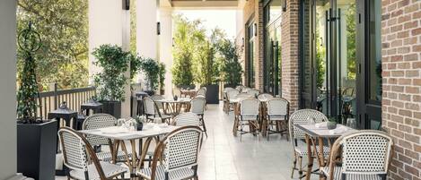 An outdoor patio with wicker tables and chairs, a brick wall, and potted plants.