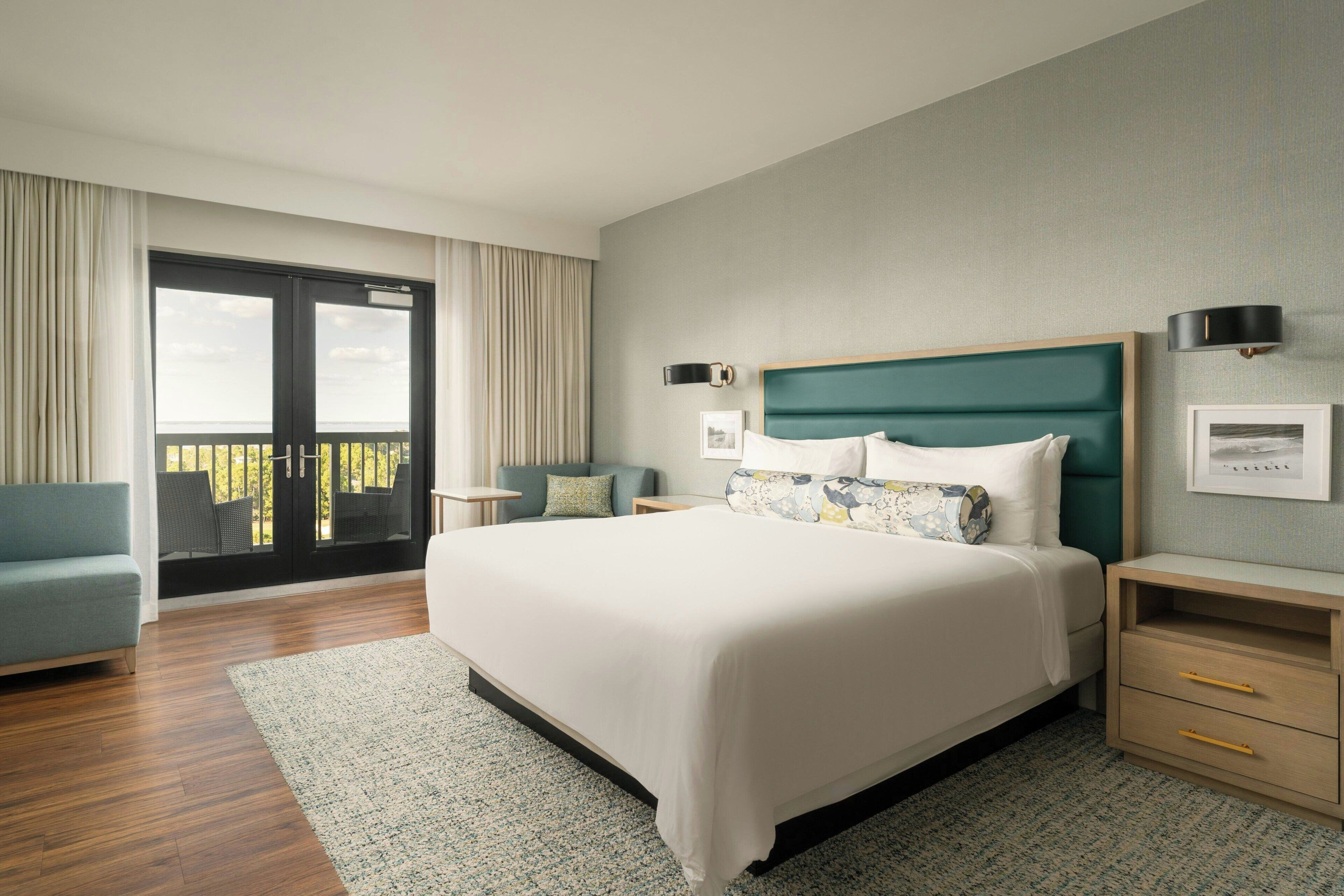 Een moderne hotelkamer met een groot bed, een balkon, een bank en een nachtkastje.