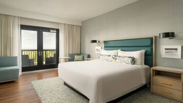 A modern hotel room with a large bed, a balcony, a sofa, and a nightstand.
