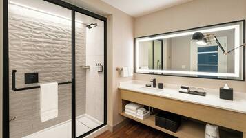 A modern bathroom with a glass shower enclosure, a large mirror, and a wooden vanity with a towel rack.