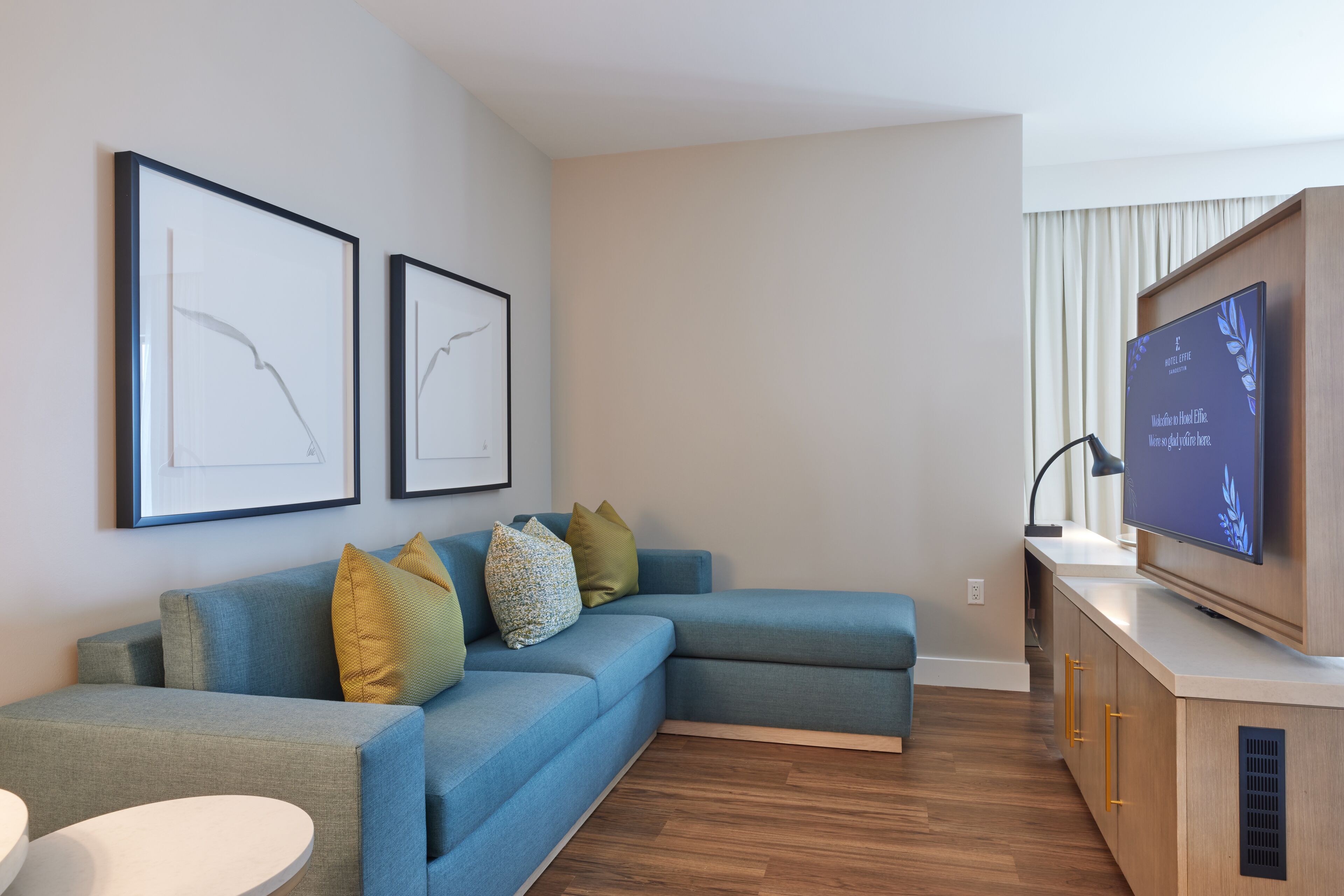 A modern living room with a sectional sofa, a flat-screen TV, and framed artwork on the wall.
