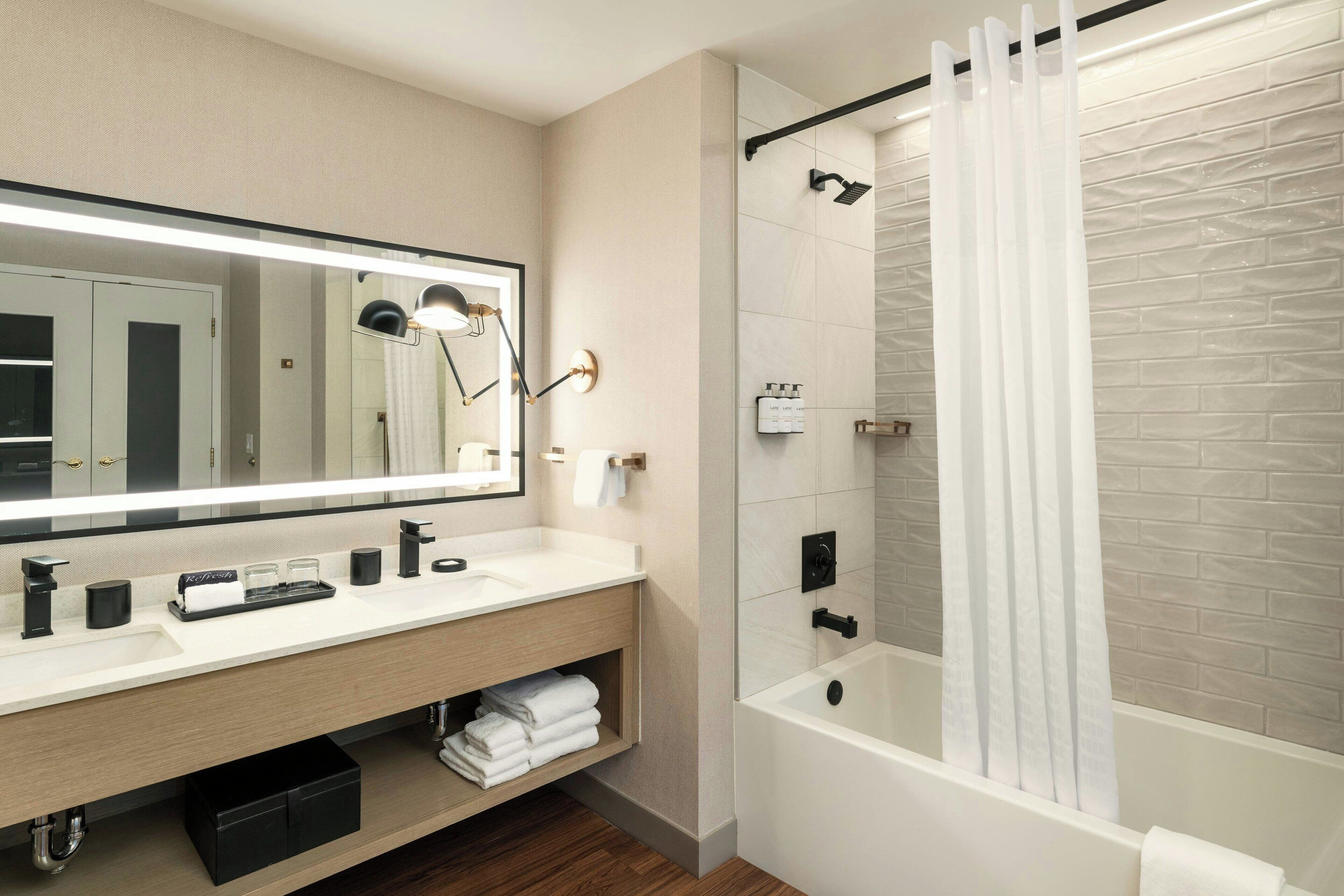 Une salle de bain moderne avec un grand miroir, un lavabo blanc, une baignoire et un rideau de douche.