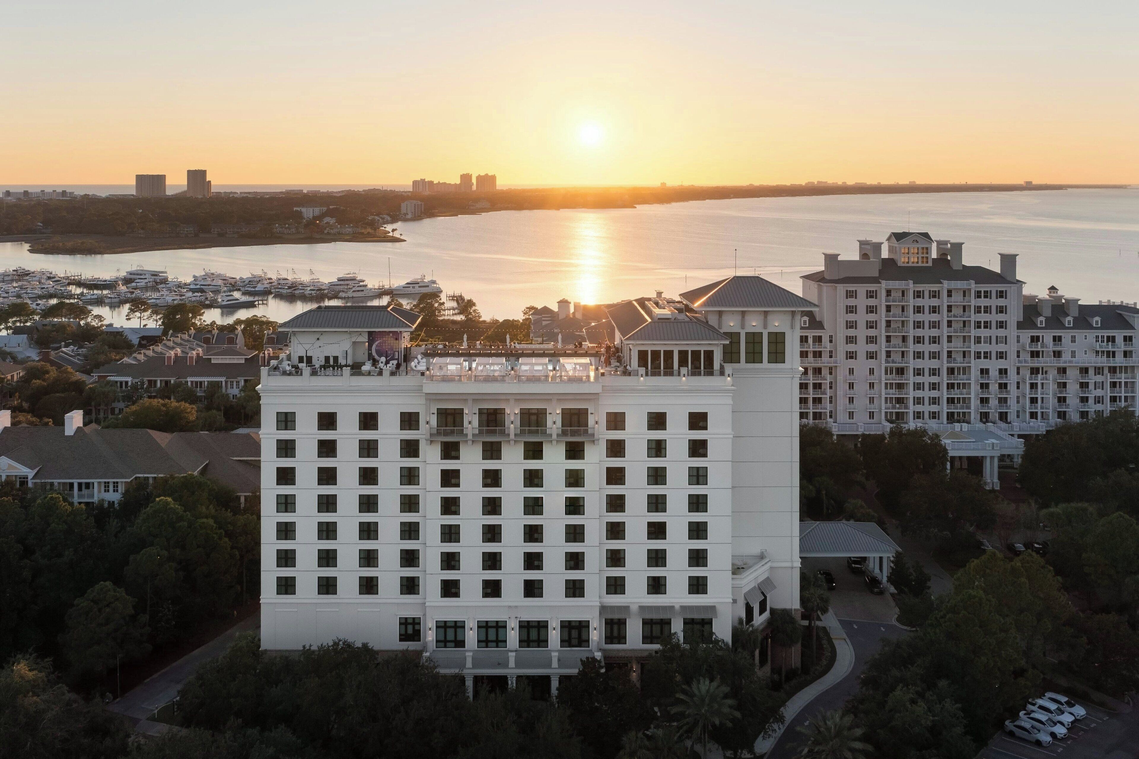 Un hotel de gran altura con varios pisos, una marina con barcos y un atardecer sobre el agua.