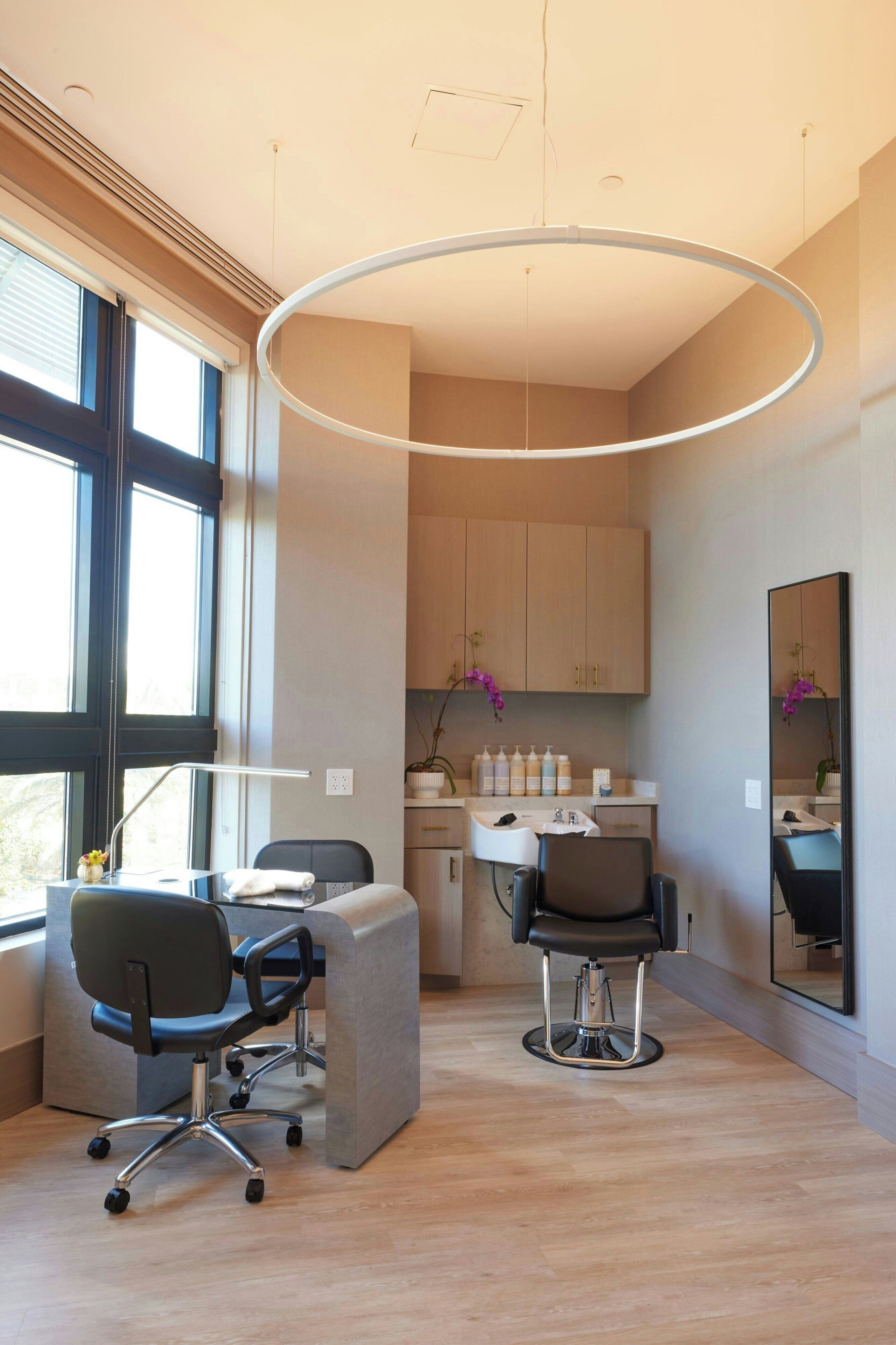 A modern hair salon with two chairs, a large mirror, and a circular light fixture.