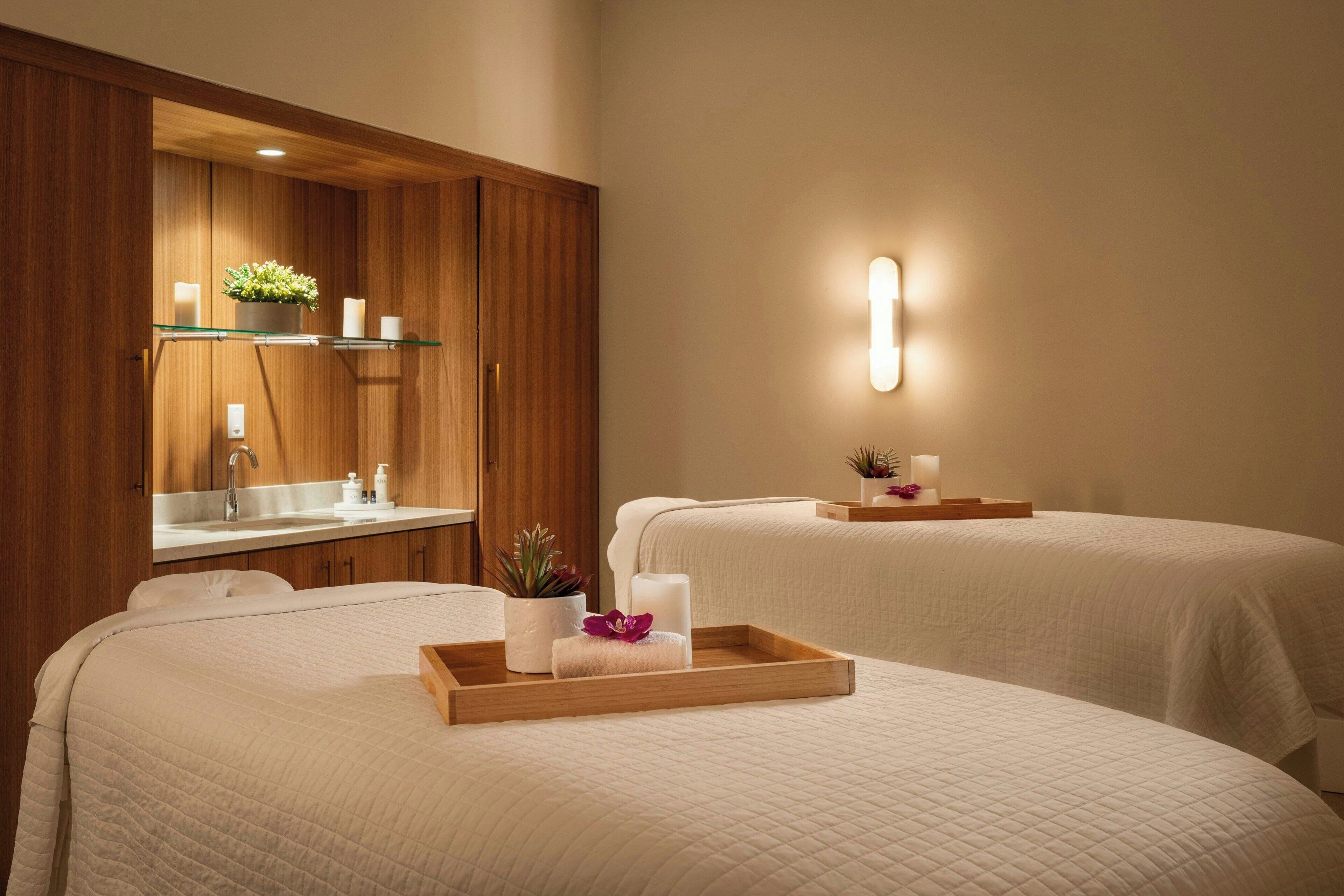 Ein Hotelzimmer mit zwei Betten, einem Holzschrank mit Spiegel, einer Glasablage für Pflegeprodukte und einer Wandleuchte.
