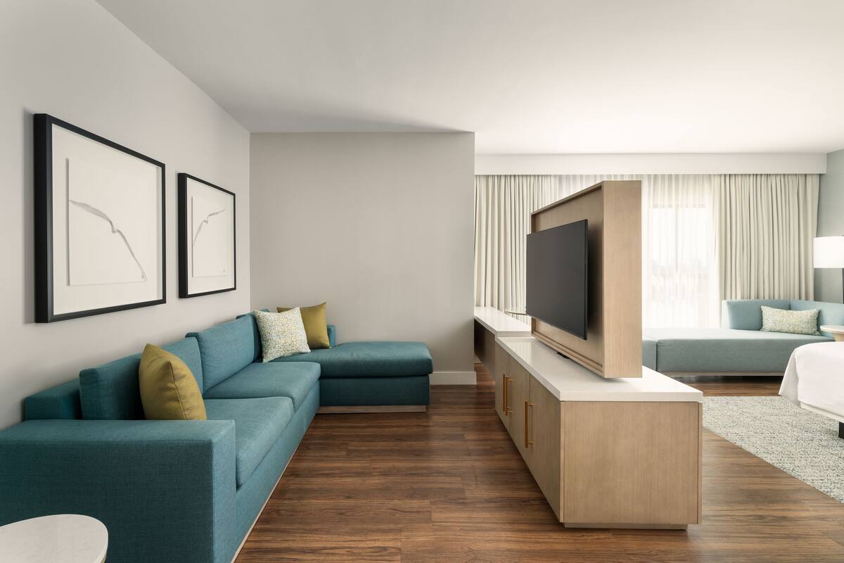 Une chambre d’hôtel moderne dotée d’un canapé d’angle, d’une télévision à écran plat et d’un espace nuit séparé.