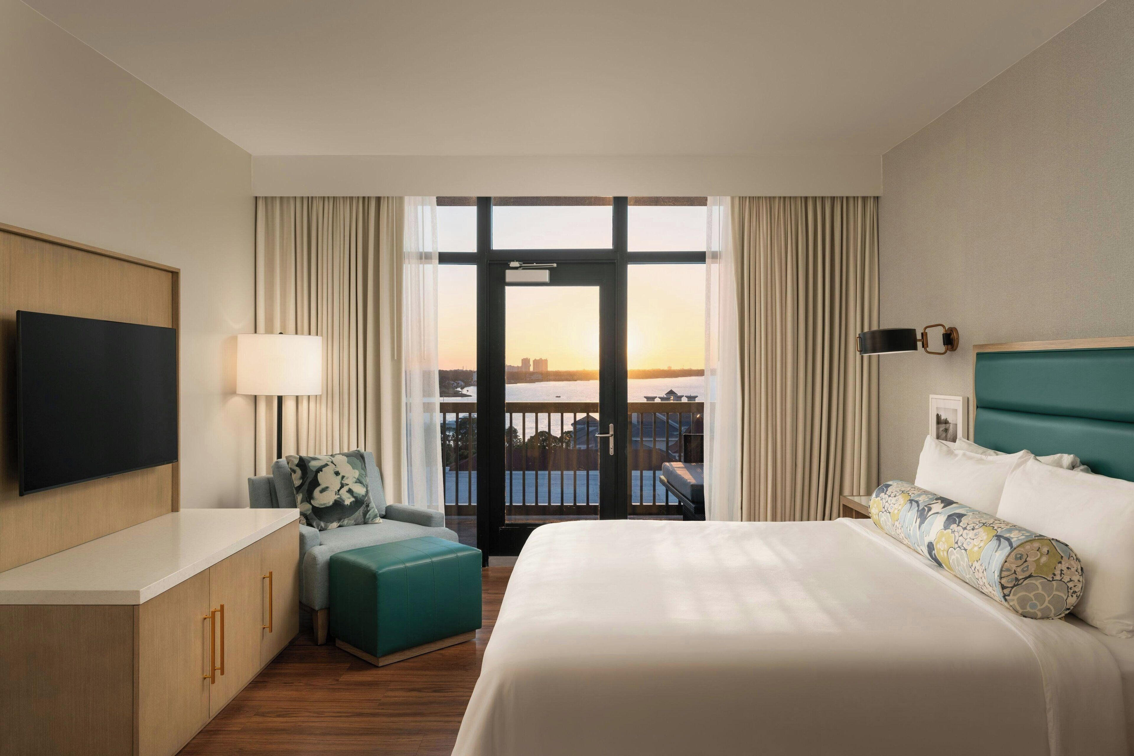 Hotelkamer met een bed, bureau, stoel, televisie en balkon met uitzicht op de stad.