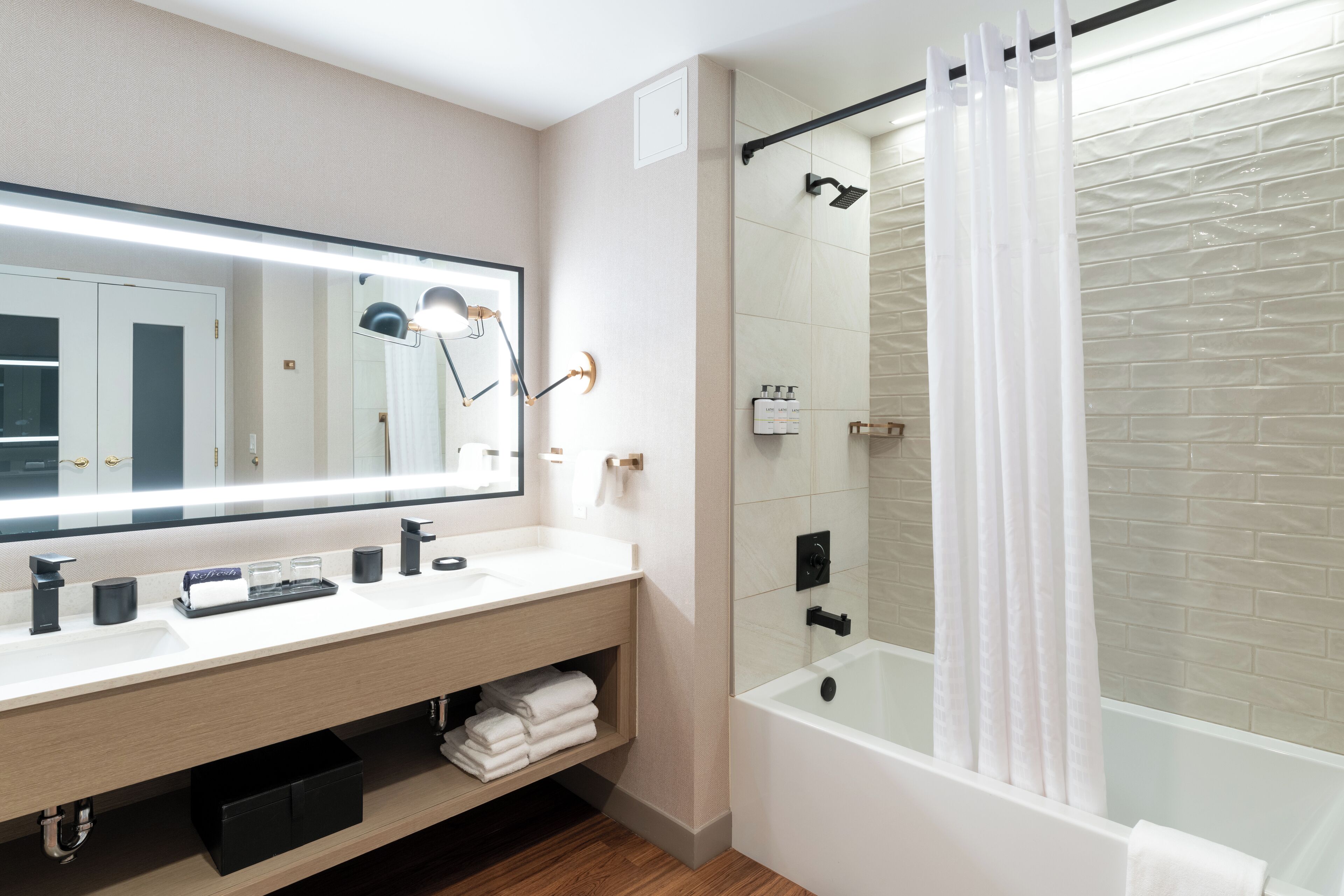 Un baño moderno con un espejo grande, lavamanos blanco y ducha con mampara de vidrio.