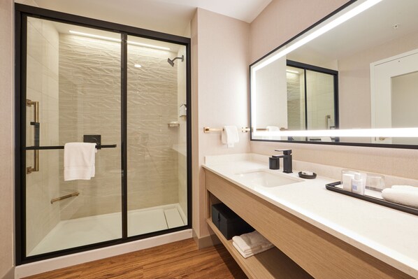 Un baño moderno con ducha envuelta en vidrio, un espejo grande y un tocador de madera con lavabo y toallero.
