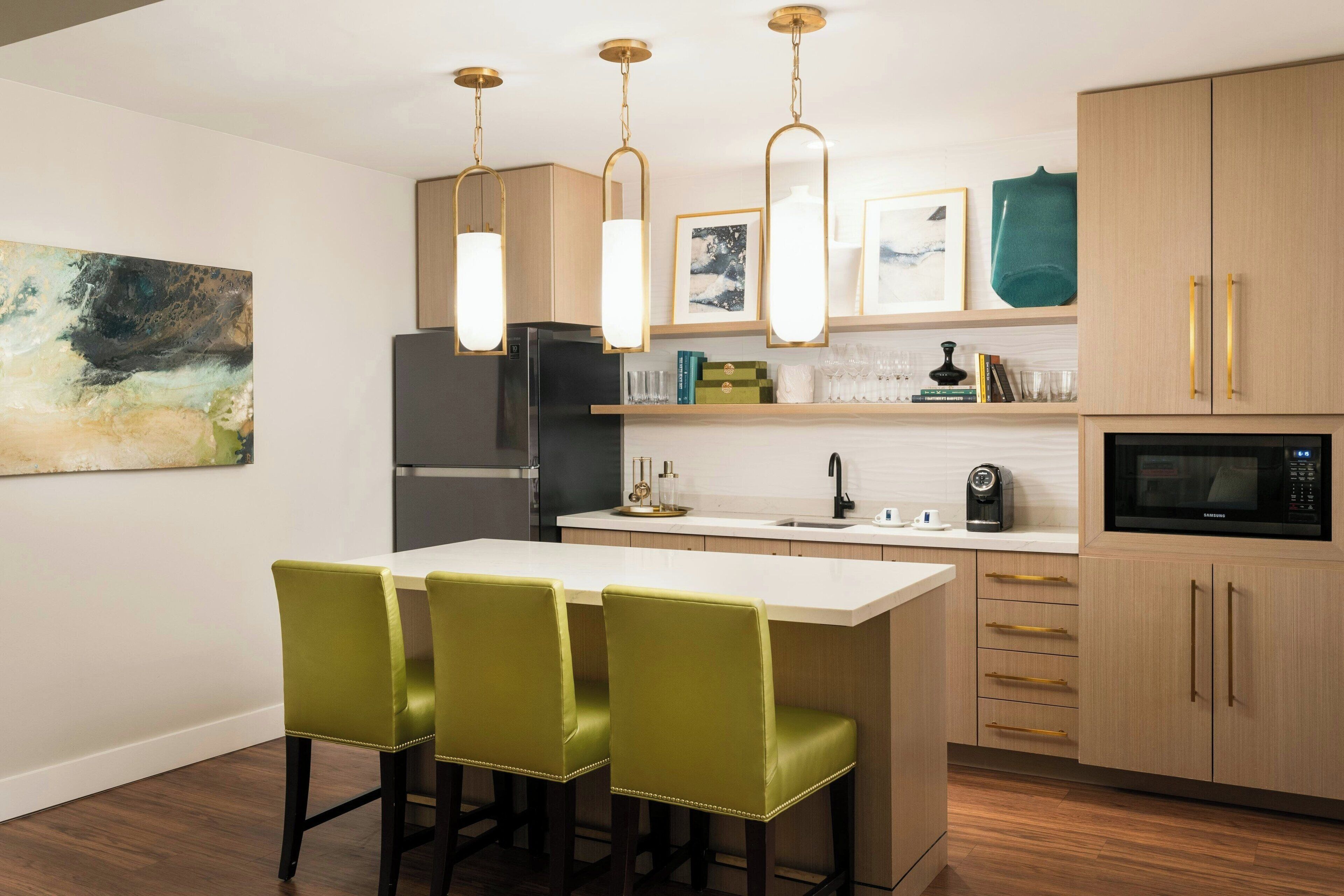 A modern kitchen with a central island, green bar stools, pendant lights, and wooden cabinets.