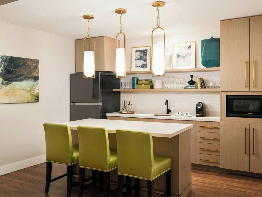Una cocina moderna con una isla central, taburetes de bar verdes, lámparas colgantes y armarios de madera.