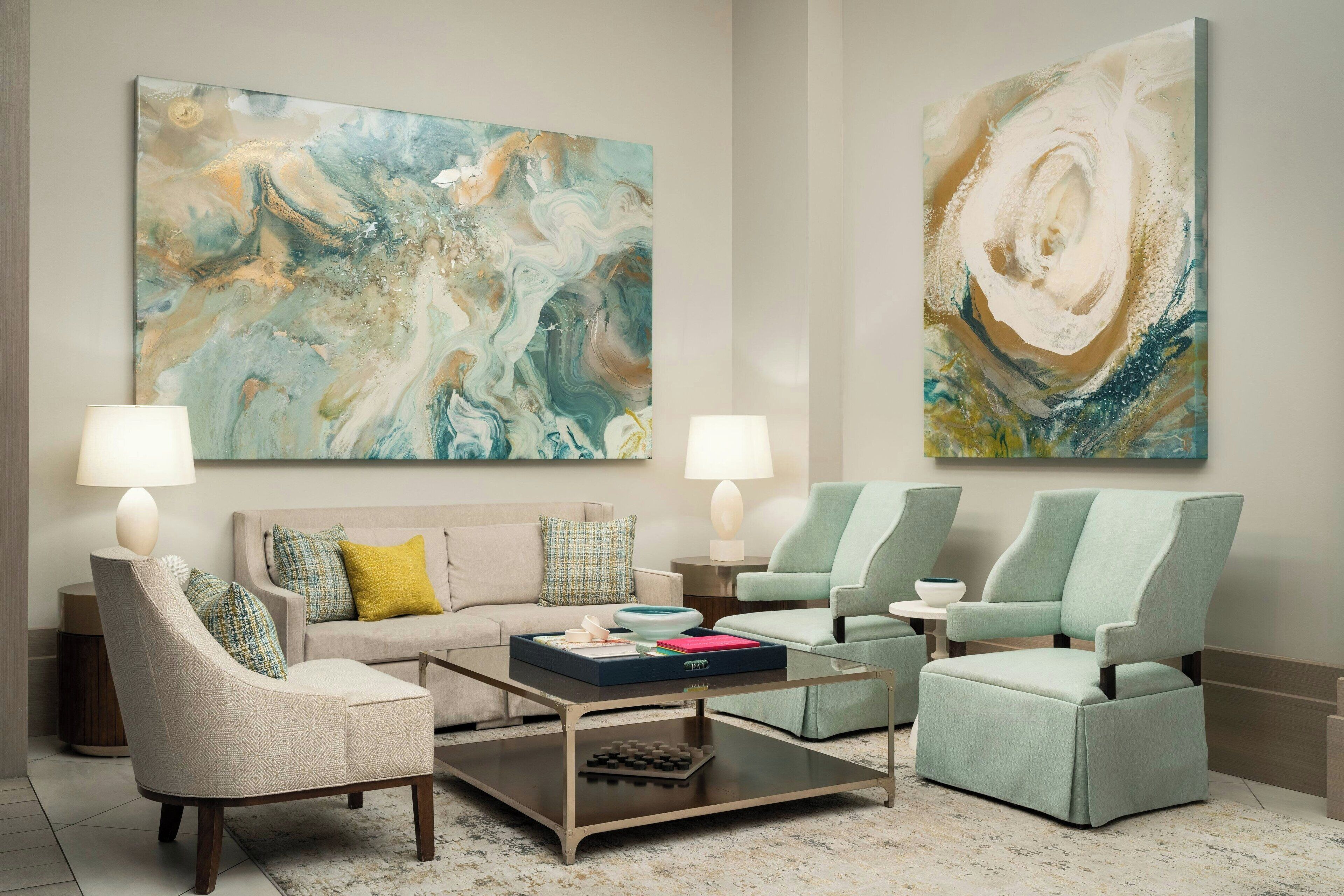 Una sala de estar moderna con sofá, sillones, una mesita de centro y dos lámparas. Hay pinturas abstractas en la pared.