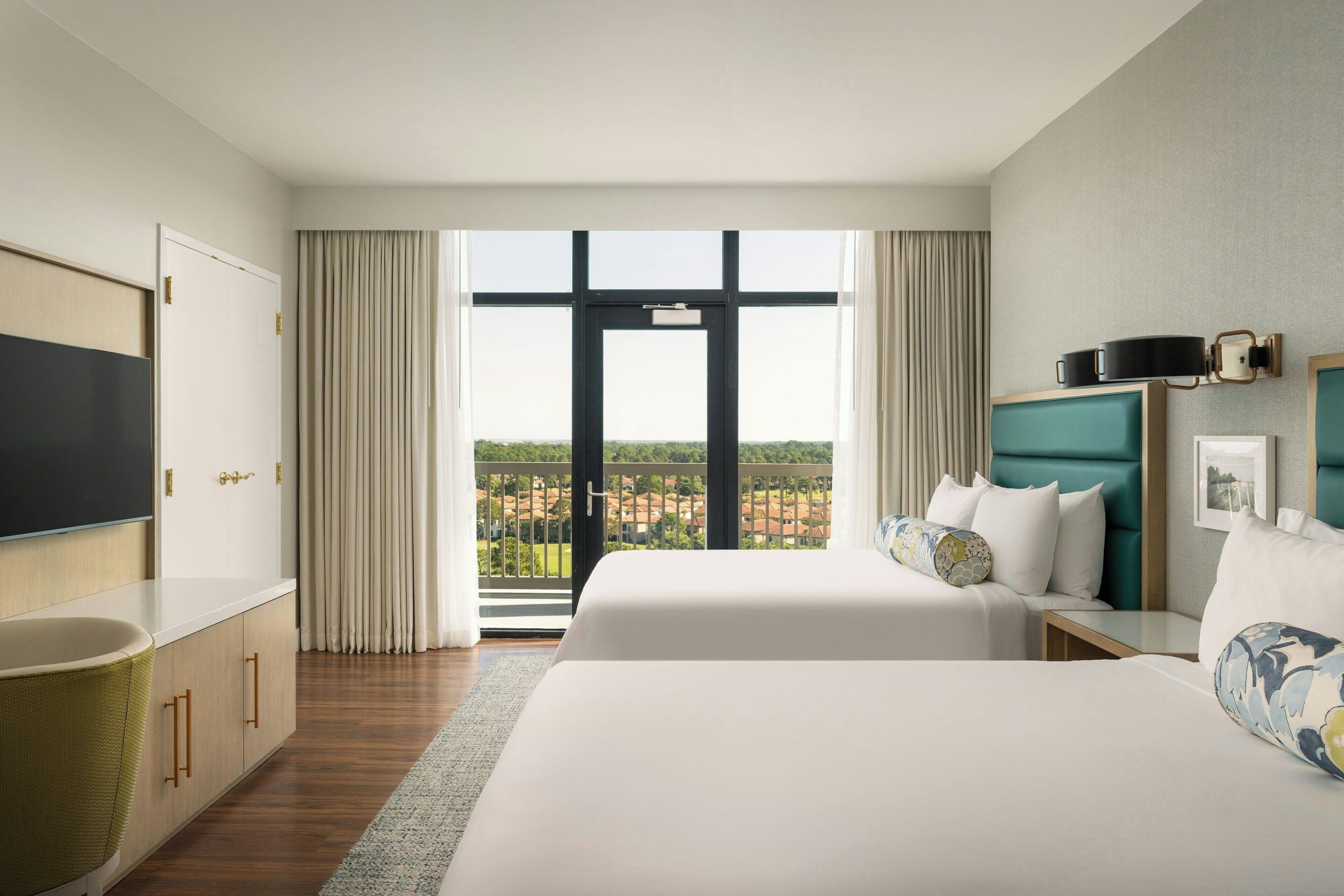 Ett hotellrum med ett stort fönster, två sängar, en TV och en minibar.