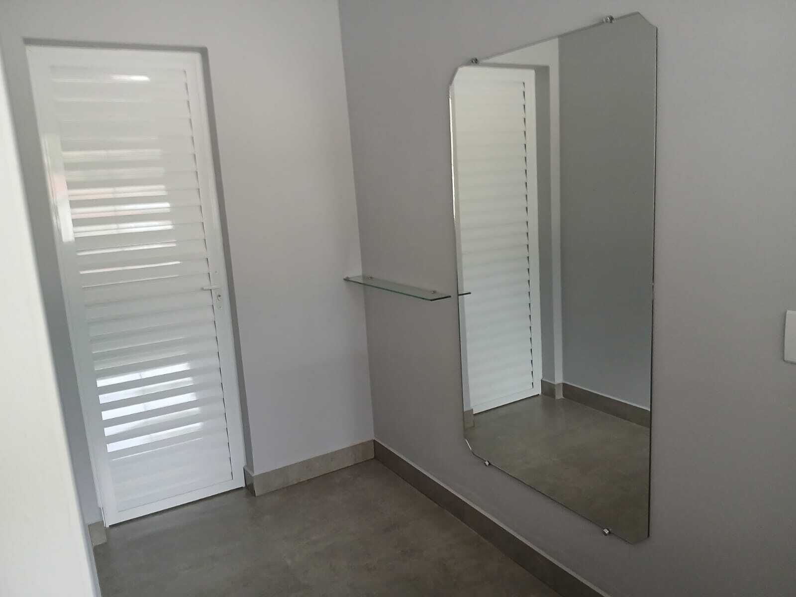 A room with a closed door, a mirror on the wall, and a small shelf.