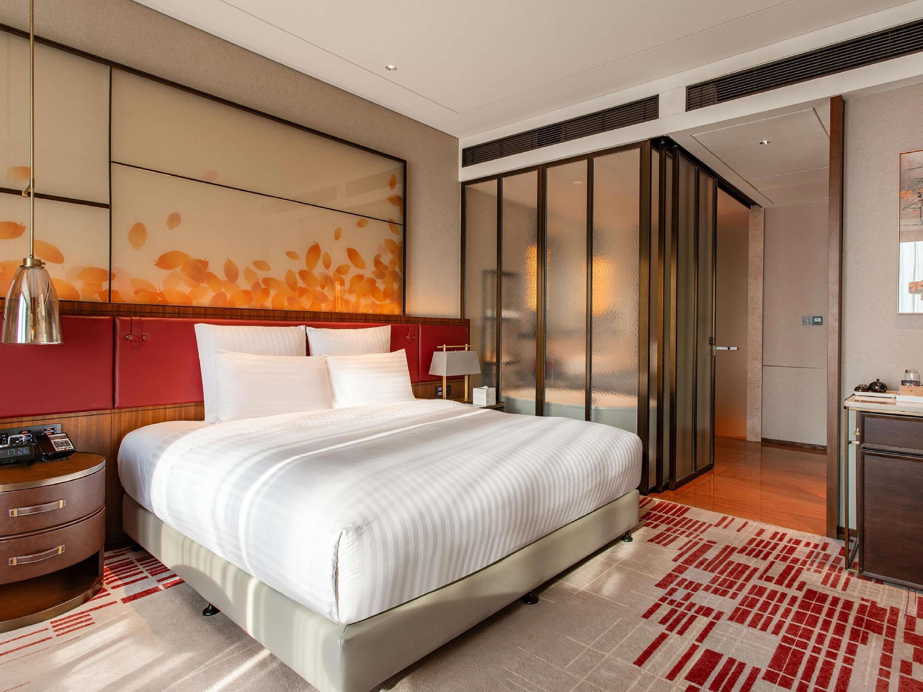 A hotel room with a large bed, a nightstand, a desk, a wardrobe, and a sliding door.