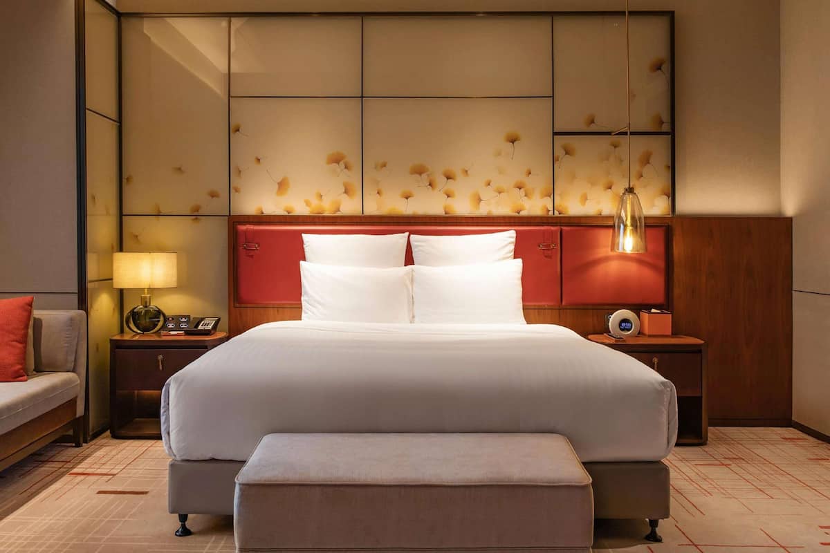 Een moderne hotelkamer met een groot bed, een nachtkastje met een lamp, een klok en een rode hoofdbord.