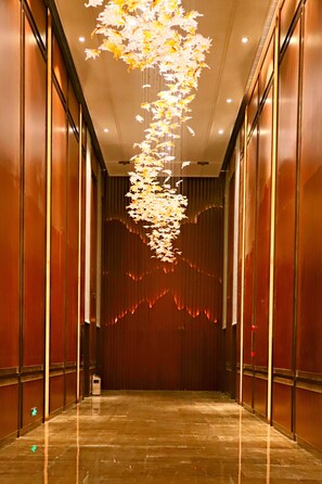 A hallway with a reflective floor, wooden panel walls, and a hanging floral light fixture.