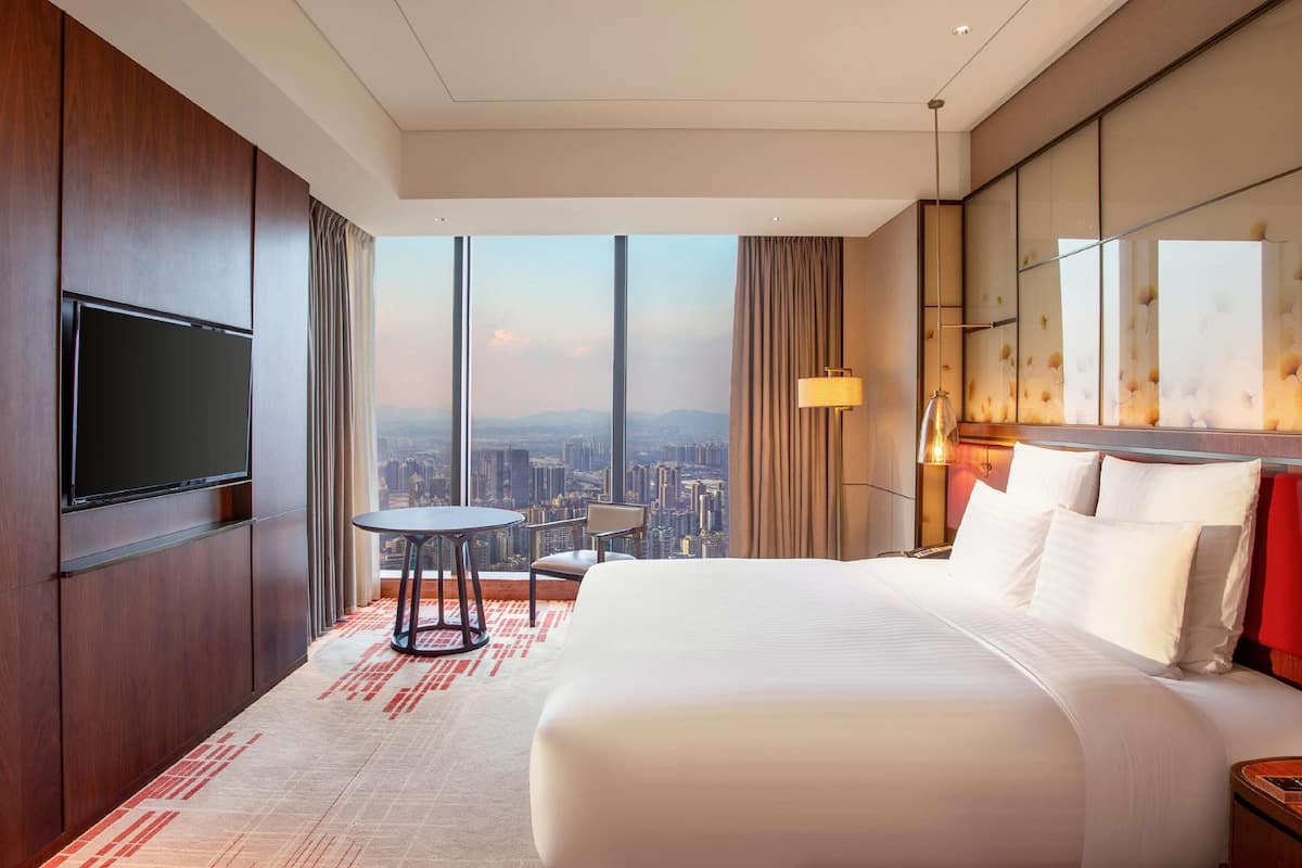 Een hotelkamer met een groot bed, een aan de muur bevestigde televisie, een klein tafeltje en uitzicht op de stad.